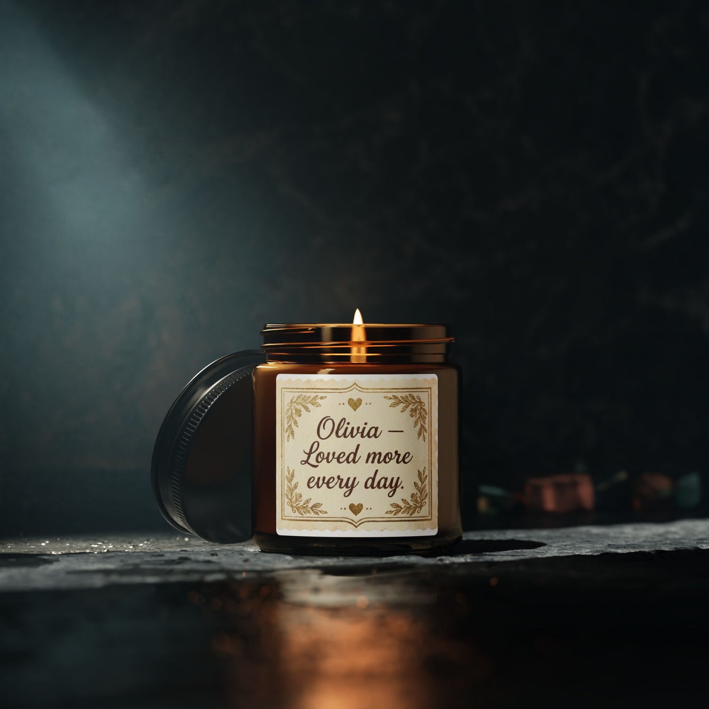 Amber glass candle with 'Olivia – Loved more every day' label on dark stone background
